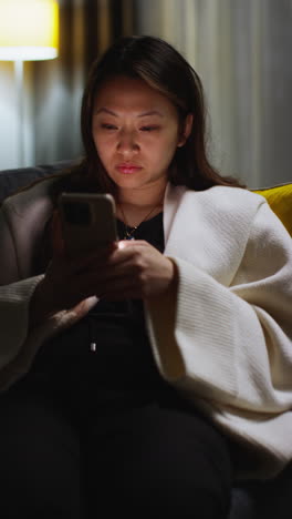 Vertical-Video-Of-Woman-Spending-Evening-At-Home-Sitting-On-Sofa-With-Mobile-Phone-Scrolling-Through-Internet-Or-Social-Media-2